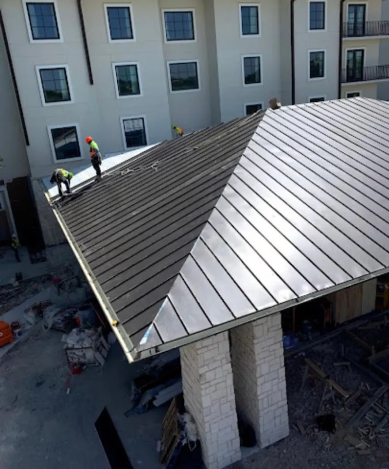 Crew installing standing seam metal roof panels on a commercial project in Barre